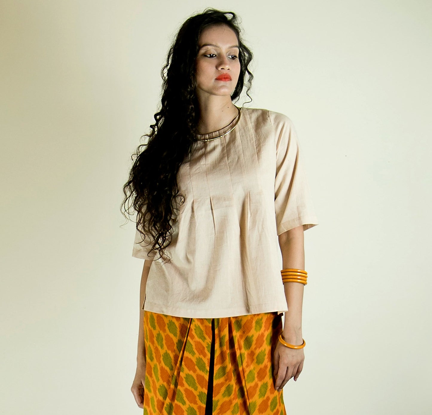 Image of woman in a light beige top paired with yellow ikkat dhoti